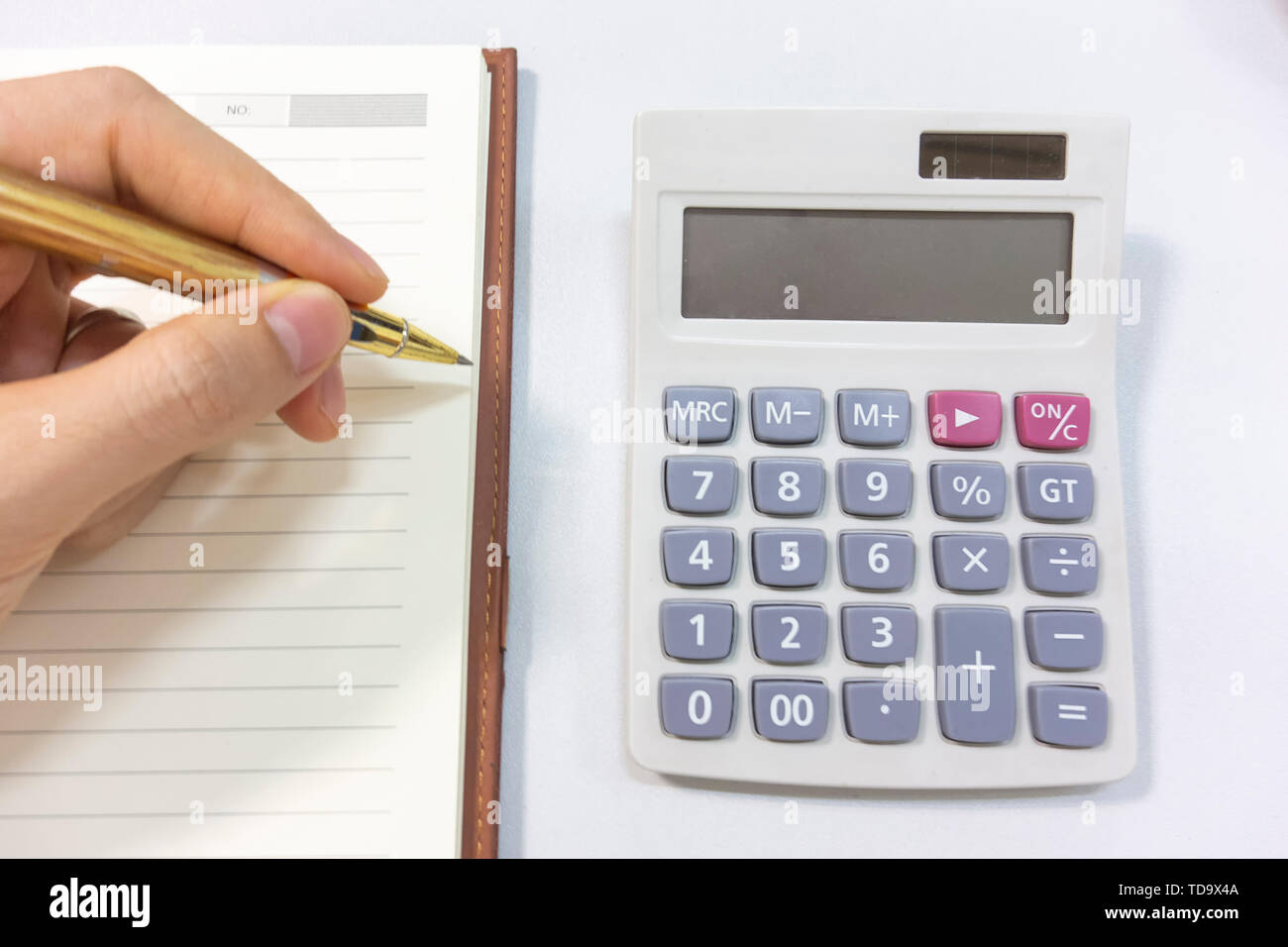 Es gibt einen Rechner durch die Hand mit einem Kugelschreiber auf dem Schreibtisch. Stockfoto