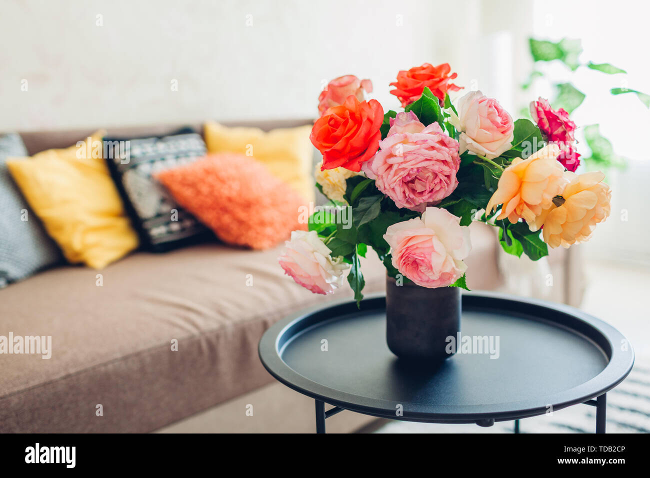 Innenraum der Wohnzimmer mit Blumen am Kaffeetisch und gemütliches Sofa mit Kissen dekoriert. Blumenstrauß aus farbenfrohen frische Rosen Stockfoto