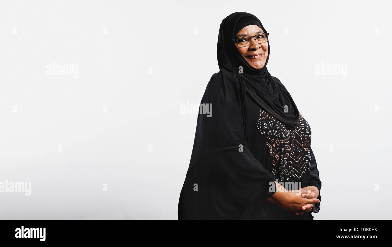 Ältere muslimische Frau im hijab auf weißem Hintergrund. Lächelnd arabische Frau in Brillen und Schwarz hijab an Kamera schaut. Stockfoto