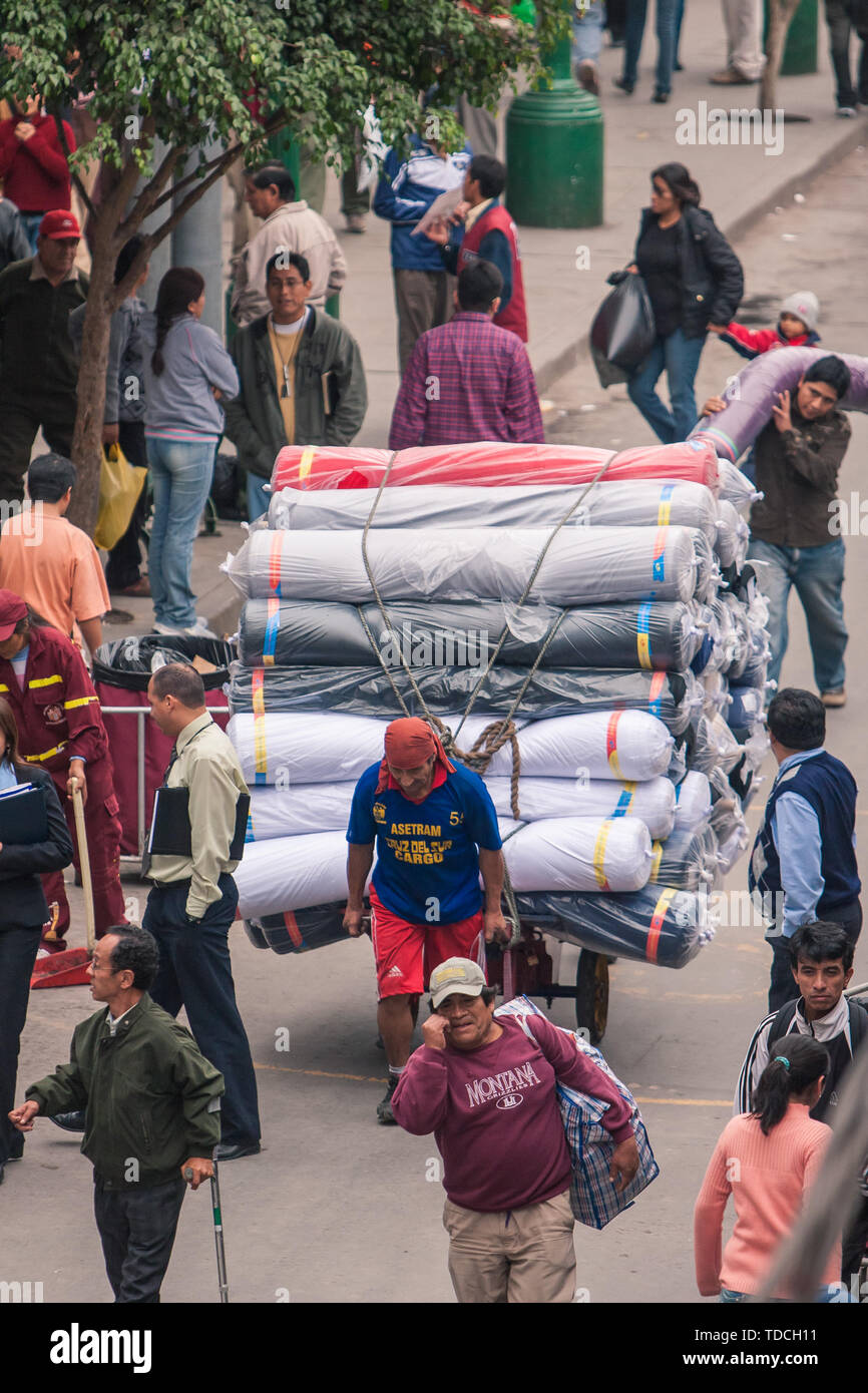 Lima/Peru Jun 13.2008: Latino Mann, der Wagen voll beladen mit Teppichen und Stoffen auf der Straße der größten Garment District genannt Gamarra. Stockfoto