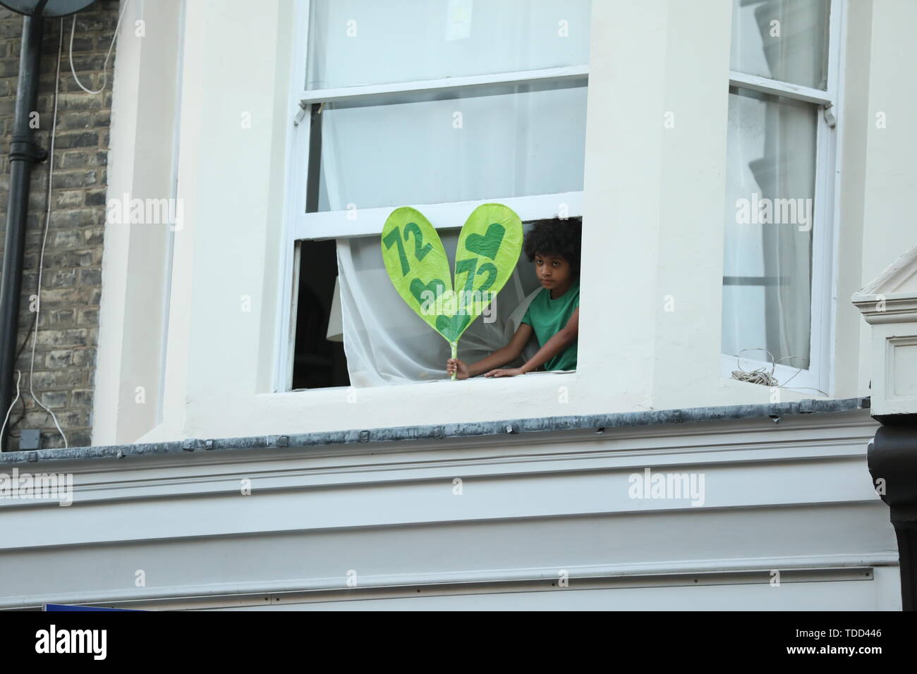 Ein Kind hält ein Plakat vor seinem Fenster, wie Familie und Freunde der 72 Menschen, die ihr Leben in der Grenfell Hochhaus Brand verloren nehmen Sie teil an einem ruhigen Spaziergang in London, anlässlich des 2-jährigen Jubiläum. Stockfoto