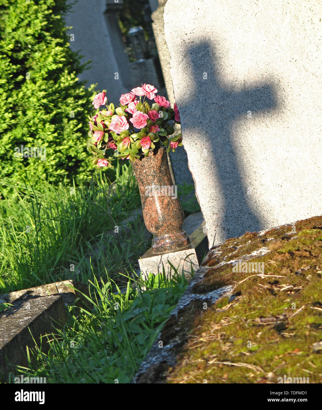 Schatten des Kreuzes auf dem Grabstein Grab mit künstlichen Blumen Stockfoto