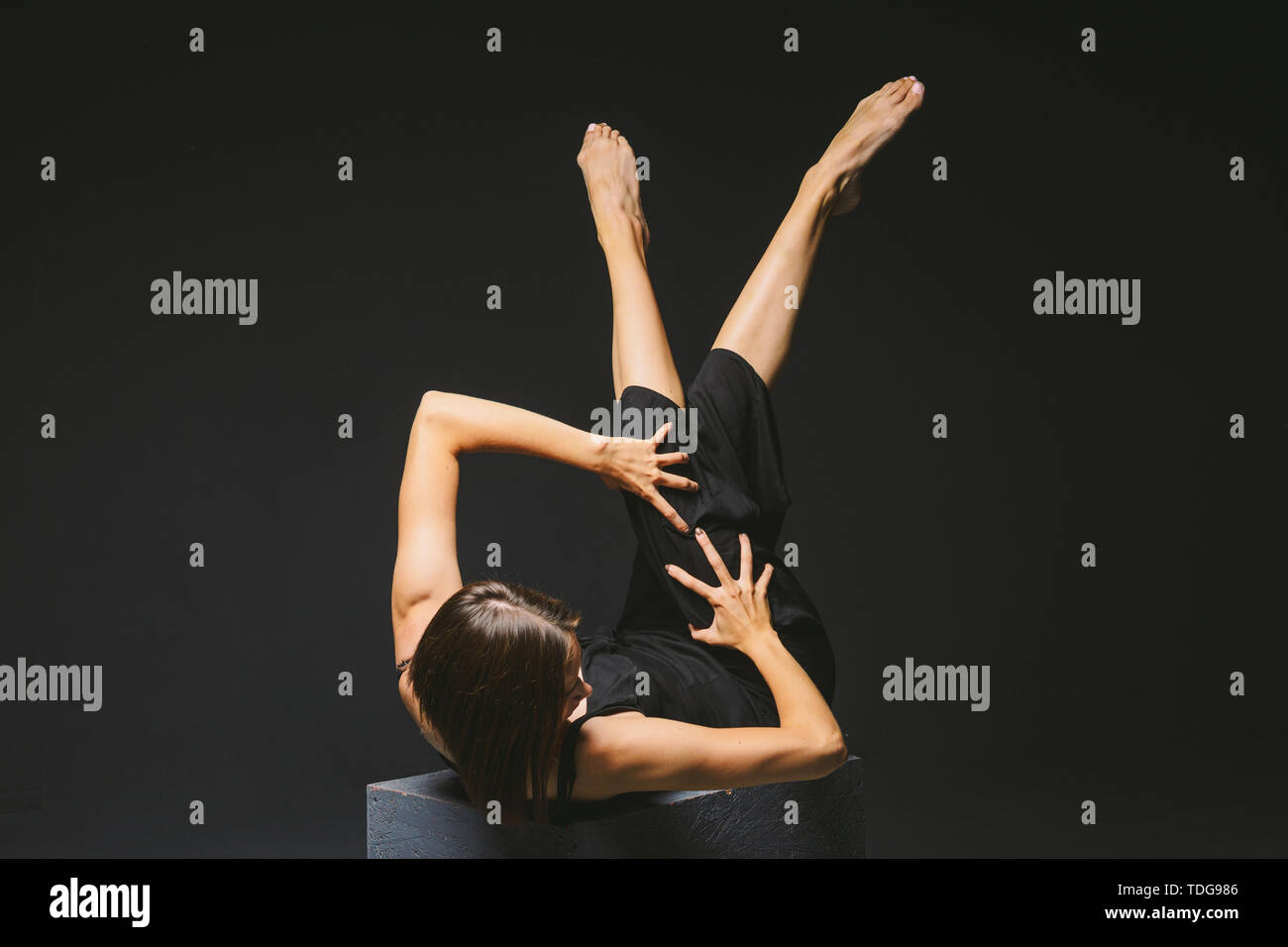 Soziale Thema. jungen kaukasischen Frau in seltsamen in Kleidung darstellen Posing auf Black Cube, dunklen Hintergrund, symbolisiert, die Schmerzen, Leiden, die Hilfe suchen, protecti Stockfoto