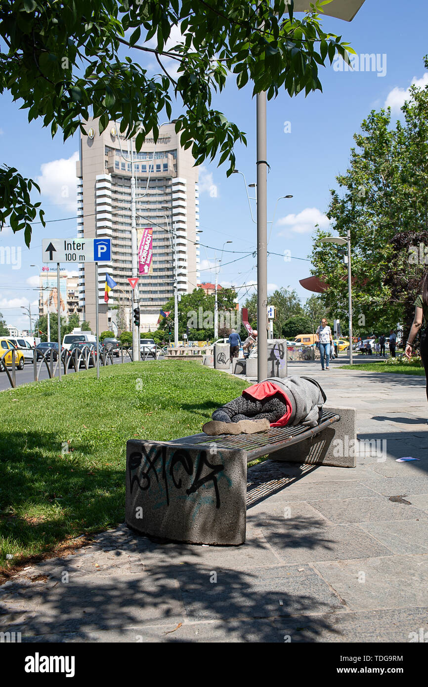 Bukarest, Rumänien - 30. Mai 2019: Antagonismus zwischen Armut und Reichtum der Innenstadt von Bukarest - armer Mann schlafen auf einer Bank an der Straße und Luxus in Stockfoto