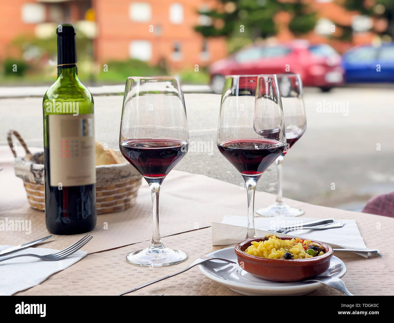 Drei Gläser Rotwein, eine Flasche Wein und Chef's Kompliment, kleine Teller Paella auf Tisch Terrasse serviert Stockfoto