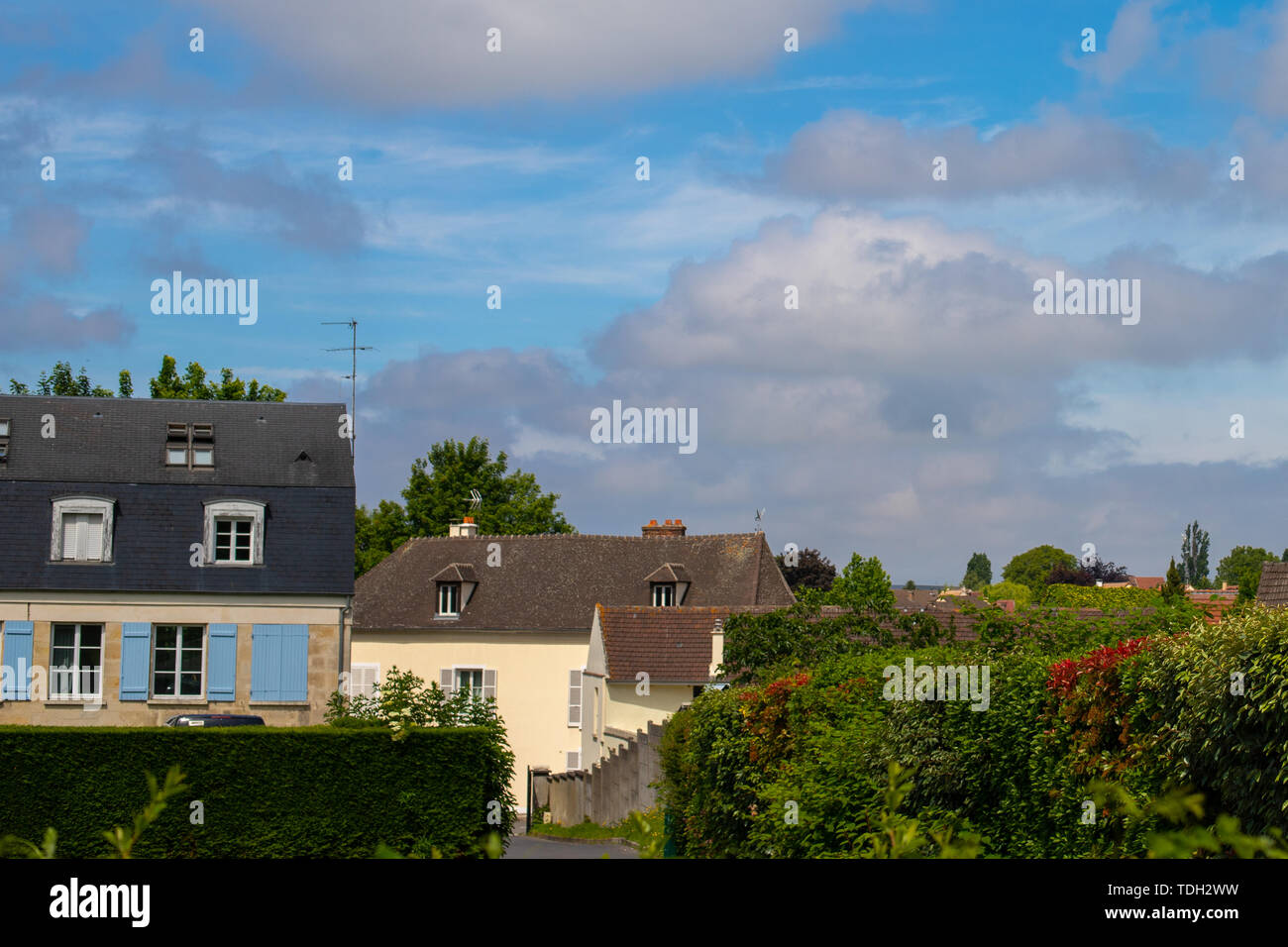Blau wolkig und kontrastierenden Himmel über einem Europäischen Dorf. Französisch Land Häuser. Hedge-fonds und viel Grün die Gasse hinunter. Stockfoto