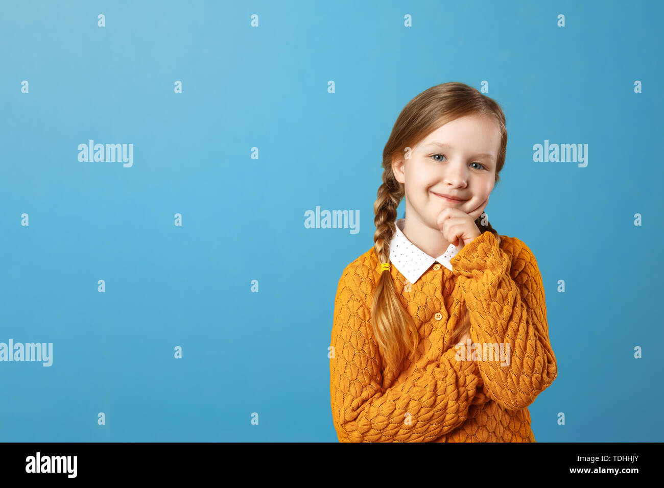 Porträt von einem kleinen Mädchen Schülerin in einem gelben Pullover auf blauem Hintergrund. Nachdenkliches Kind die Hand am Kinn und Kamera. Platz kopieren Stockfoto