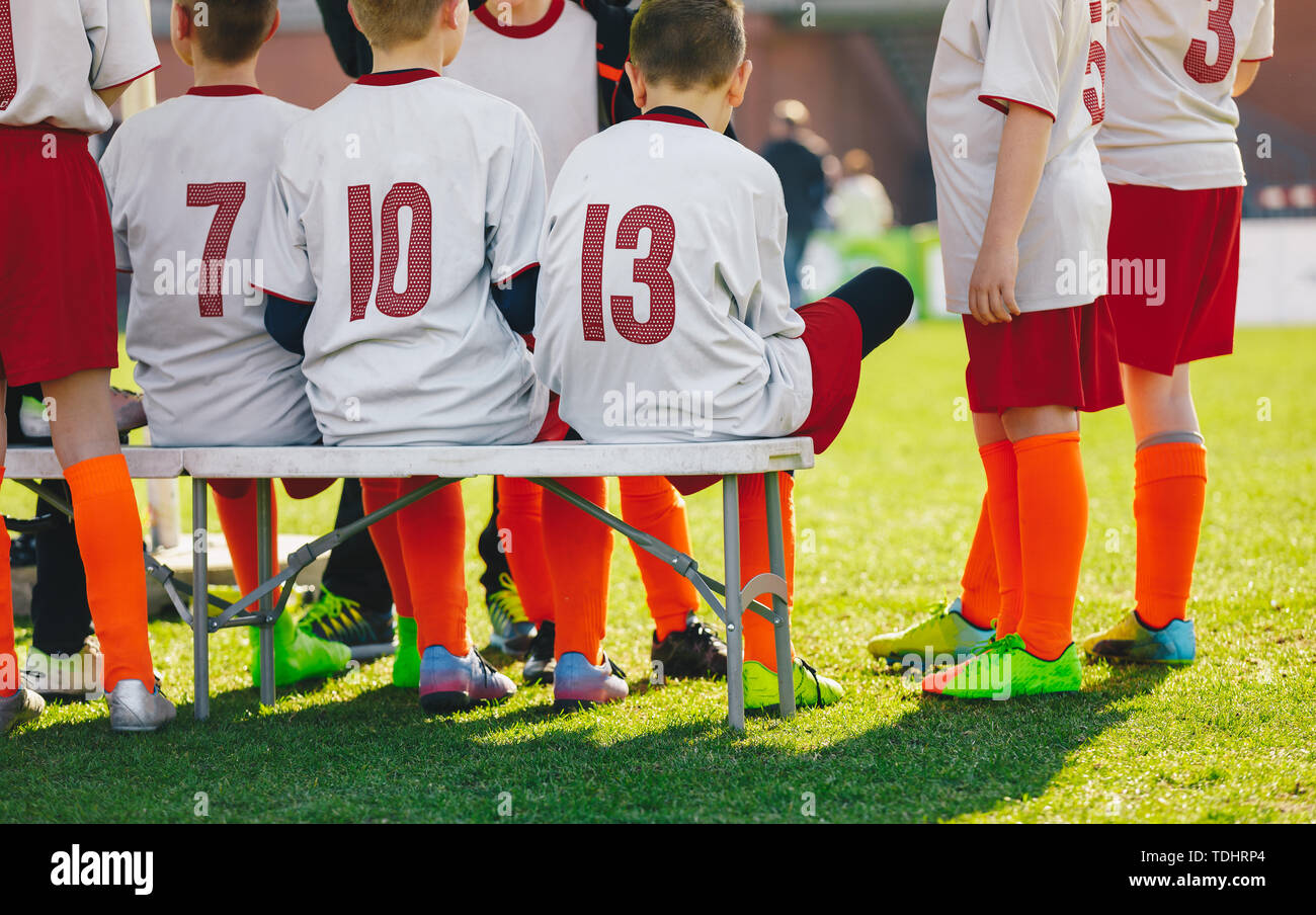 Gruppe von Kindern sitzen auf Sport Sitzbank auf Gras Schule Veranstaltungsort. Jungen in der Fußballmannschaft sitzen auf Ersatz Sitzbank Stockfoto