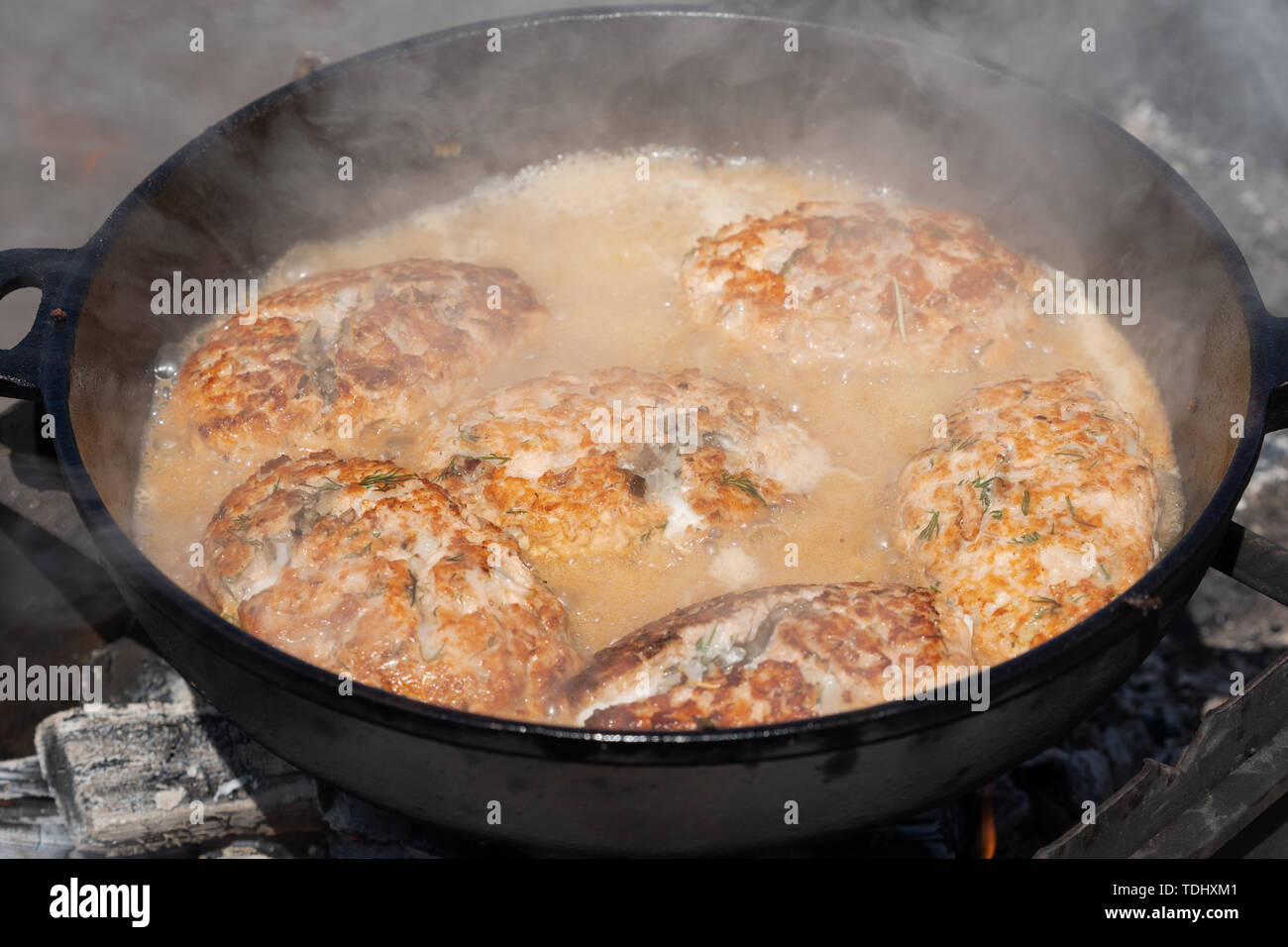Köstliche Wild Rot Lachs Fisch Schnitzel mit Soße gebraten in heißen Bratpfanne braten auf Kohlen, über offenem Feuer am Lagerfeuer. Kochen auf Feuer während Picknick o Stockfoto