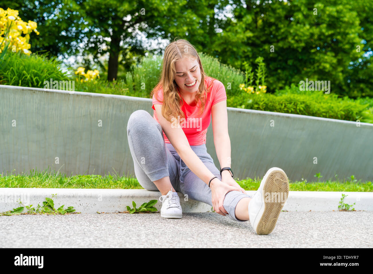 Eine junge Frau sitzt auf dem Boden, ihr verletztes Bein Holding Stockfoto