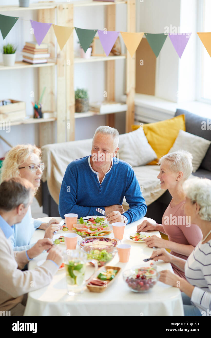 Zufrieden reifer Mann im blauen Pullover am Tisch sitzen und hören Nachrichten von Freunden beim Abendessen, Gelegenheit Freunde zu sammeln Stockfoto
