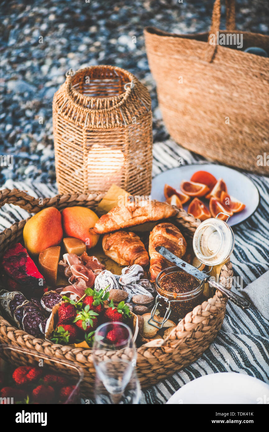 Sommer Picknick am Strand bei Sonnenuntergang. Korb voller leckeren Vorspeisen, Gebäck, Beeren und Obst der Saison auf gestreifte Decke am Strand, selektiven Fokus Stockfoto