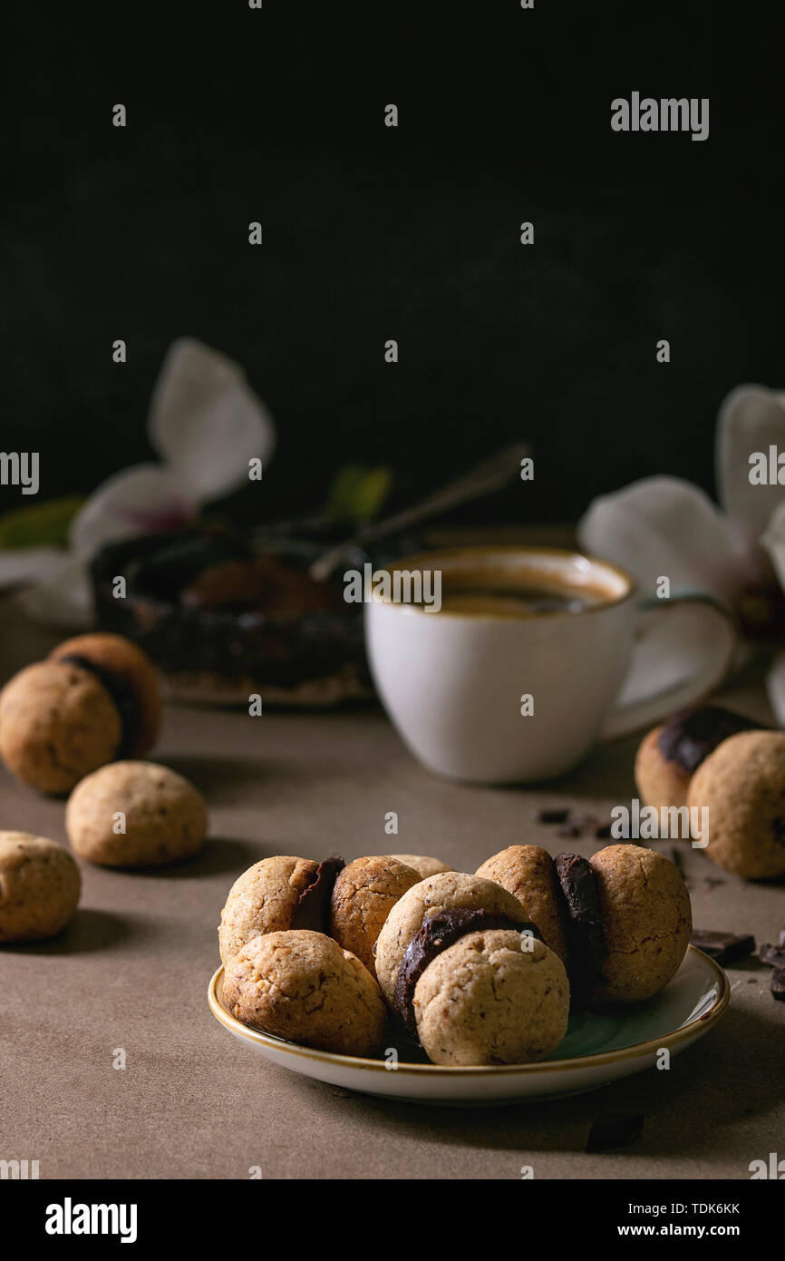 Baci di dama hausgemachte italienische Haselnuss Kekse Kekse mit Schokolade in Keramik Platte mit Tasse Espresso und Magnolia Blumen serviert. Stockfoto