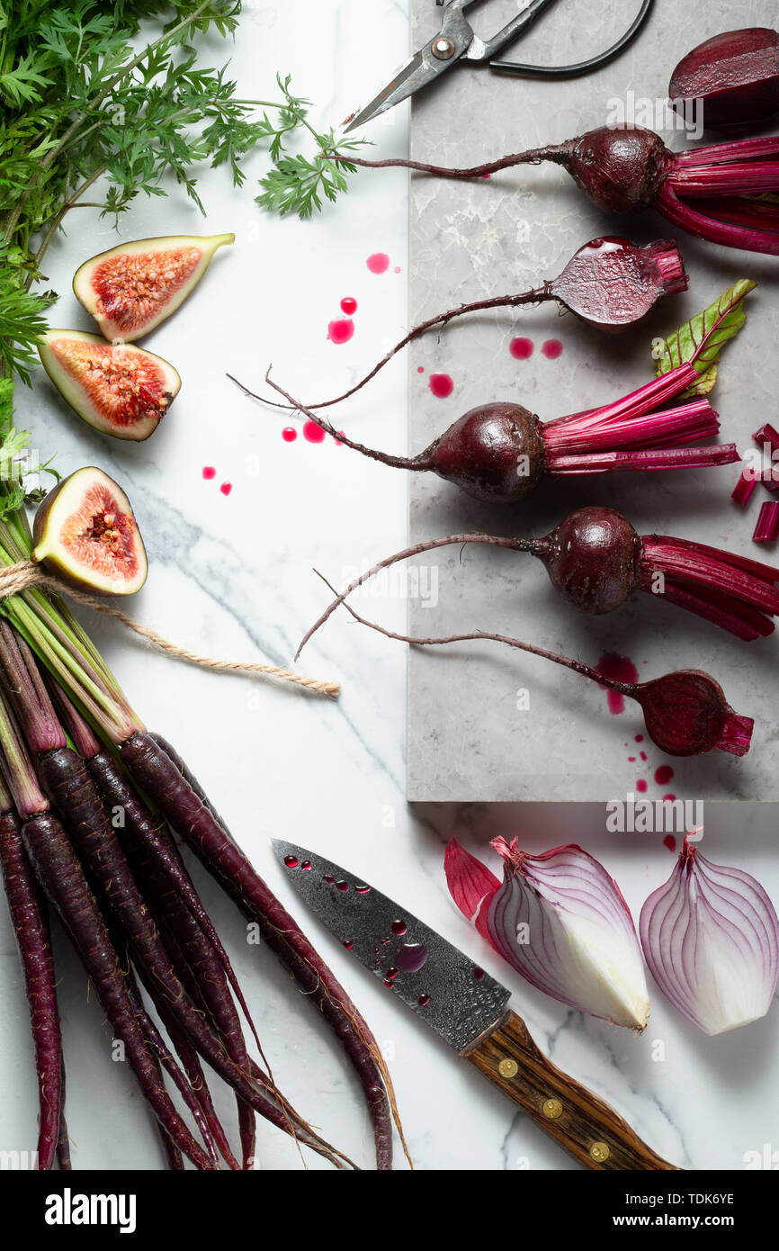 Baby, rote Beete, Karotten Lila, Lila Zwiebeln und Feigen, in Scheiben geschnitten, und auf einem Marmor Fliesen Oberfläche bereit. Ein Messer, Schere und einem Marmorbad board i Stockfoto