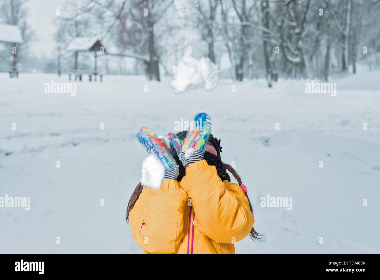 Kleines Mädchen in gelber Jacke mit wirft Schnee Winter Stockfoto