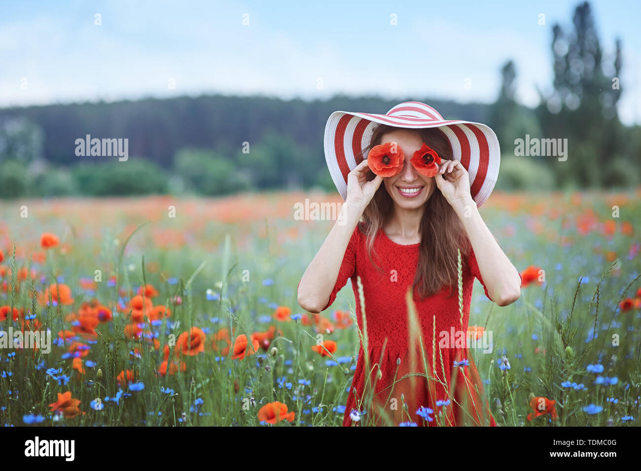 Schöne junge Frau mit roter Mohn der vor ihren Augen und in der Blumenwiese Stockfoto