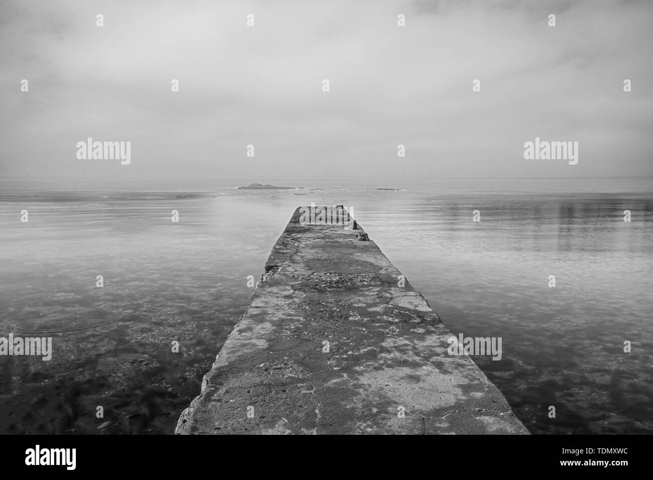 Holzsteg auf Meer und Himmel Reflexion auf dem Wasser. Lange Belichtung und schwarz-weiß Foto Stockfoto
