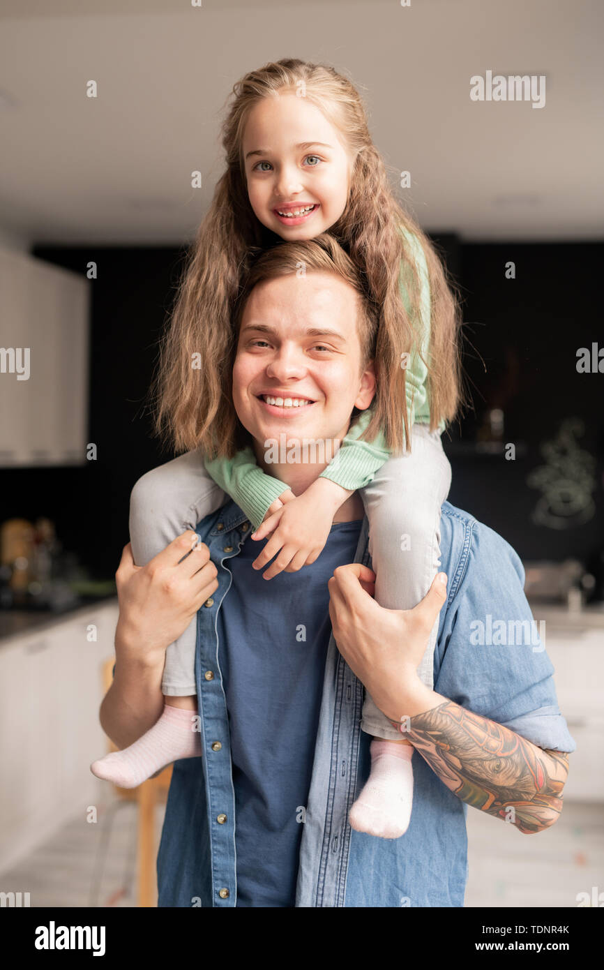 Gerne schöne Tochter mit langen Haaren sitzen auf Väter Hals und ihn umarmt, während Sie an der Kamera auf der Suche Stockfoto