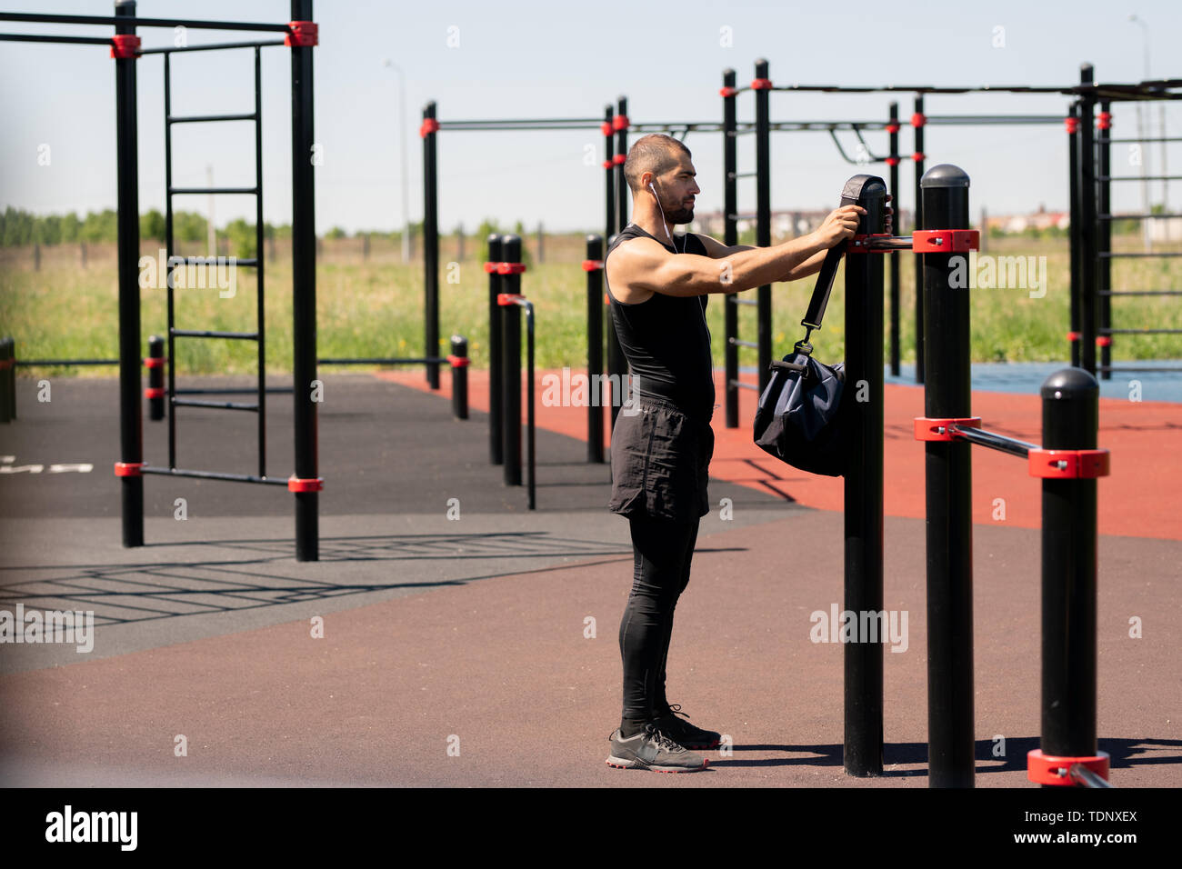 Junge muskulöse Sportler in Activewear setzt seine Tasche auf einen der Sportanlagen vor Outdoor Training Stockfoto