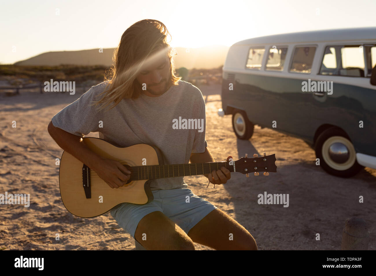 Junger Mann Gitarre spielen in der Nähe von Camper am Strand Stockfoto