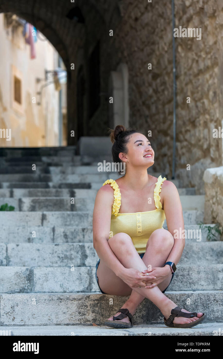 Eine junge weibliche Touristische sitzt auf Treppenstufen bis zu betrachten; Cefalu, Sizilien, Italien Stockfoto