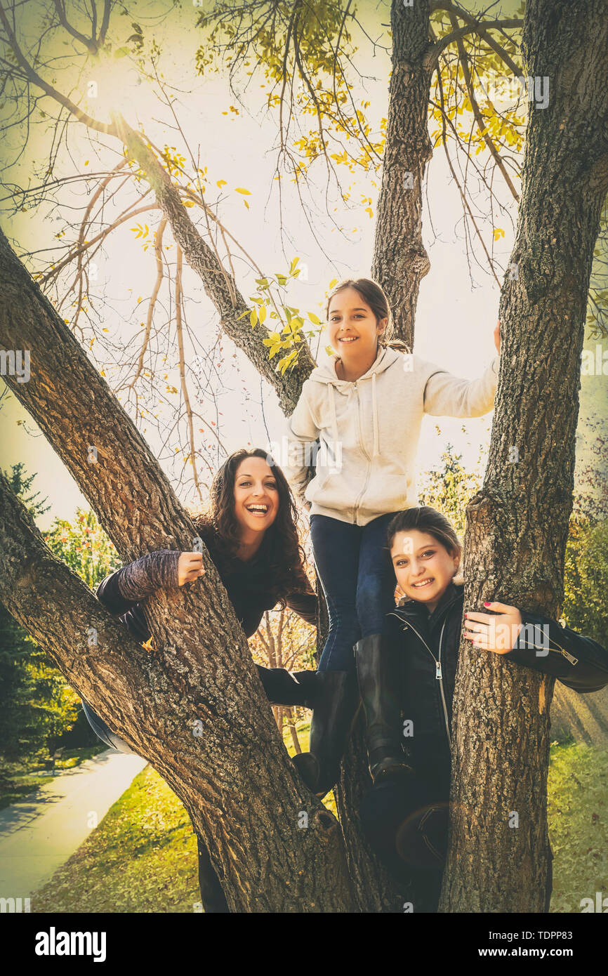 Eine Mutter und ihre zwei Töchter für eine Familie Portrait nach dem Klettern auf einen Baum in einer Stadt Park an einem warmen Herbst Tag posieren; Edmonton, Alberta, Kanada Stockfoto