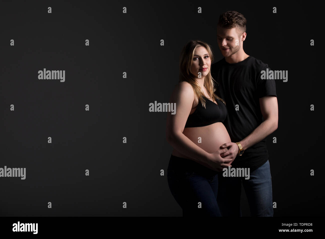 Ein junges Paar mit der Mutter, die auf die Kamera schaut, während sie ihren Bauch in einem Studio auf schwarzem Hintergrund hält: Edmonton, Albert... Stockfoto