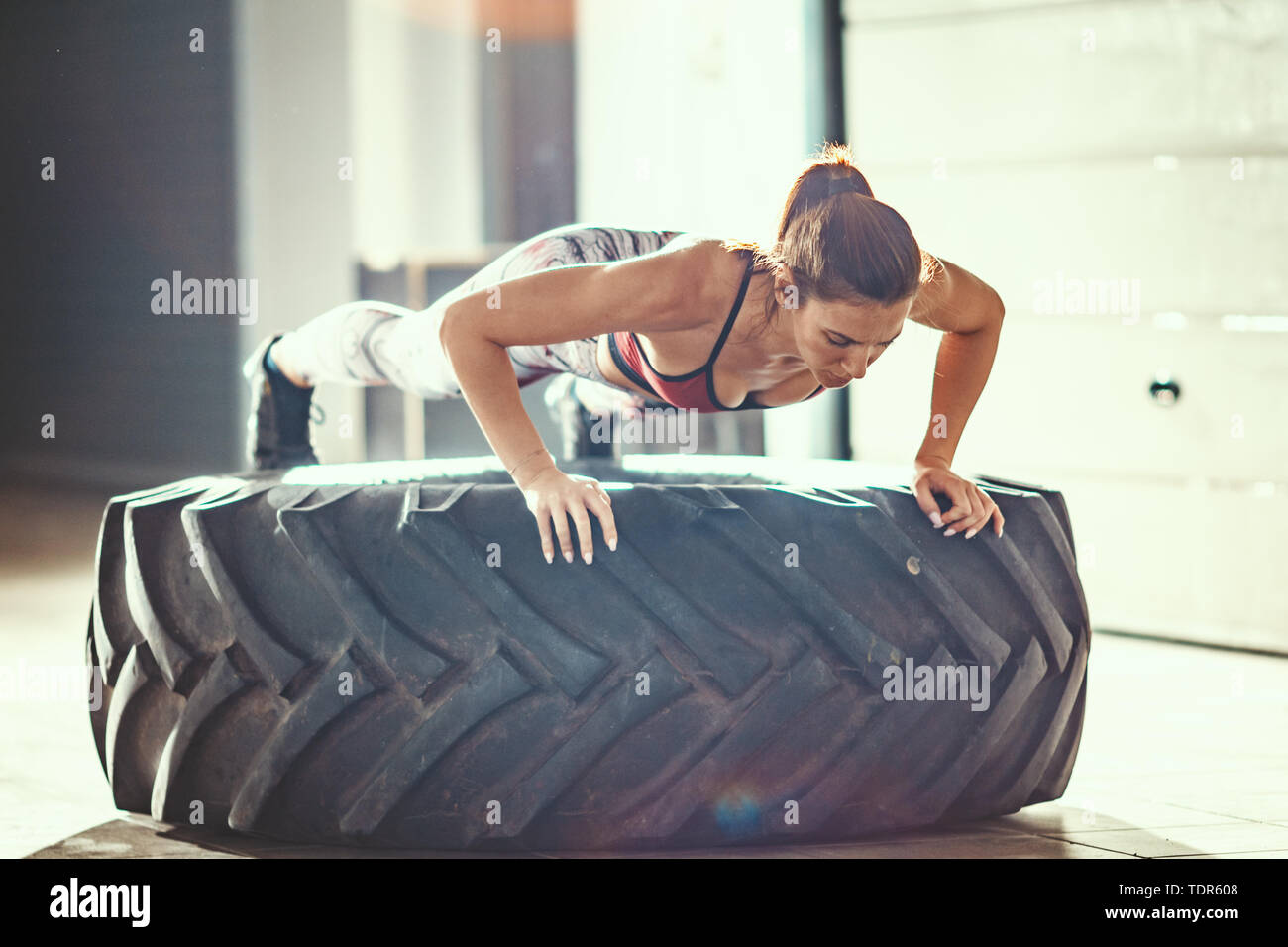 Junge muskulöse Frau tut, Push-up-Übung auf ein Reifen cross fit Training in der Garage. Stockfoto