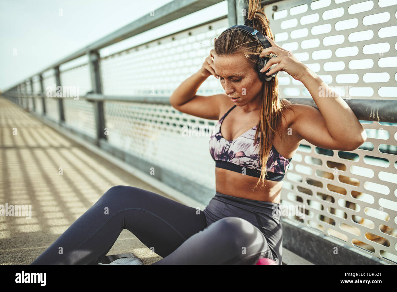 Junge fitness Frau ruht sich nach harten Training auf der Brücke über den Fluss und setzt Ihre Ohrhörer. Stockfoto