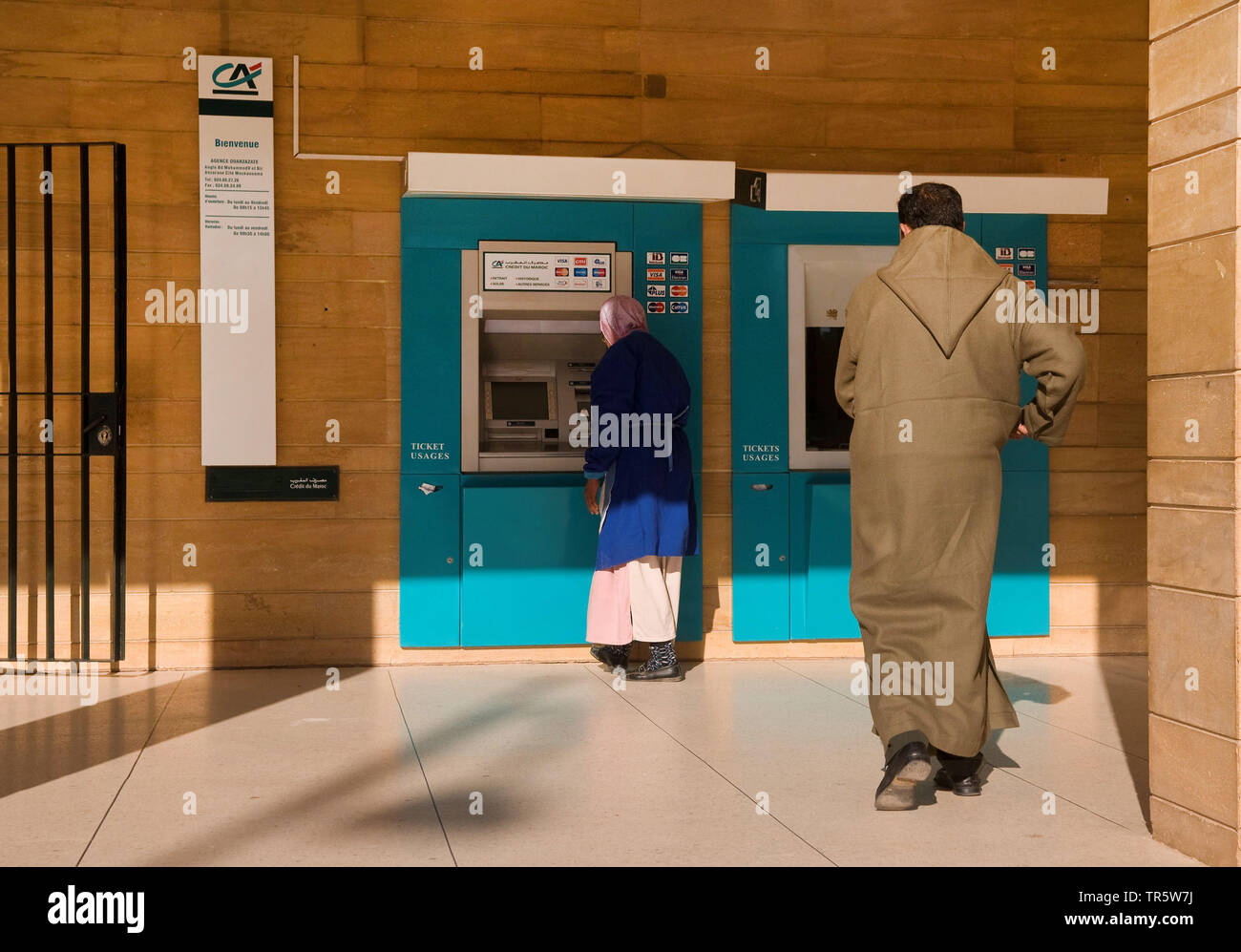 Frau mit Kopftuch und Mann, der an einem Geldautomaten, Marokko, Quarzazate Stockfoto