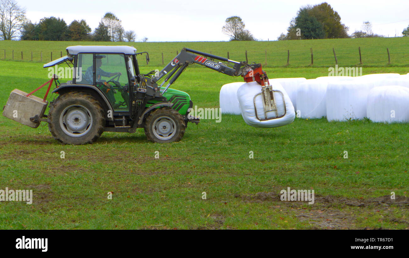 Traktor auf einer Wiese mit Silageballen, Deutschland Stockfoto