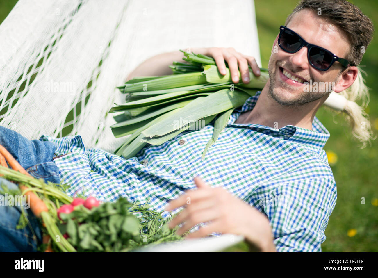 Mann liegen in einer Hängematte mit Lauch, Karotten und Radieschen, Deutschland Stockfoto