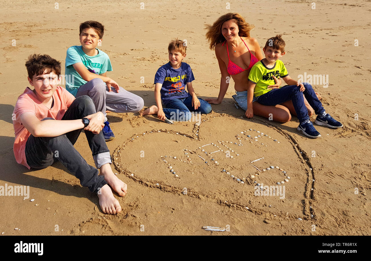 Kinder sitzen mit ihrer Mutter am Strand und feiern Mutter ┤ s Geburtstag, Niederlande Stockfoto