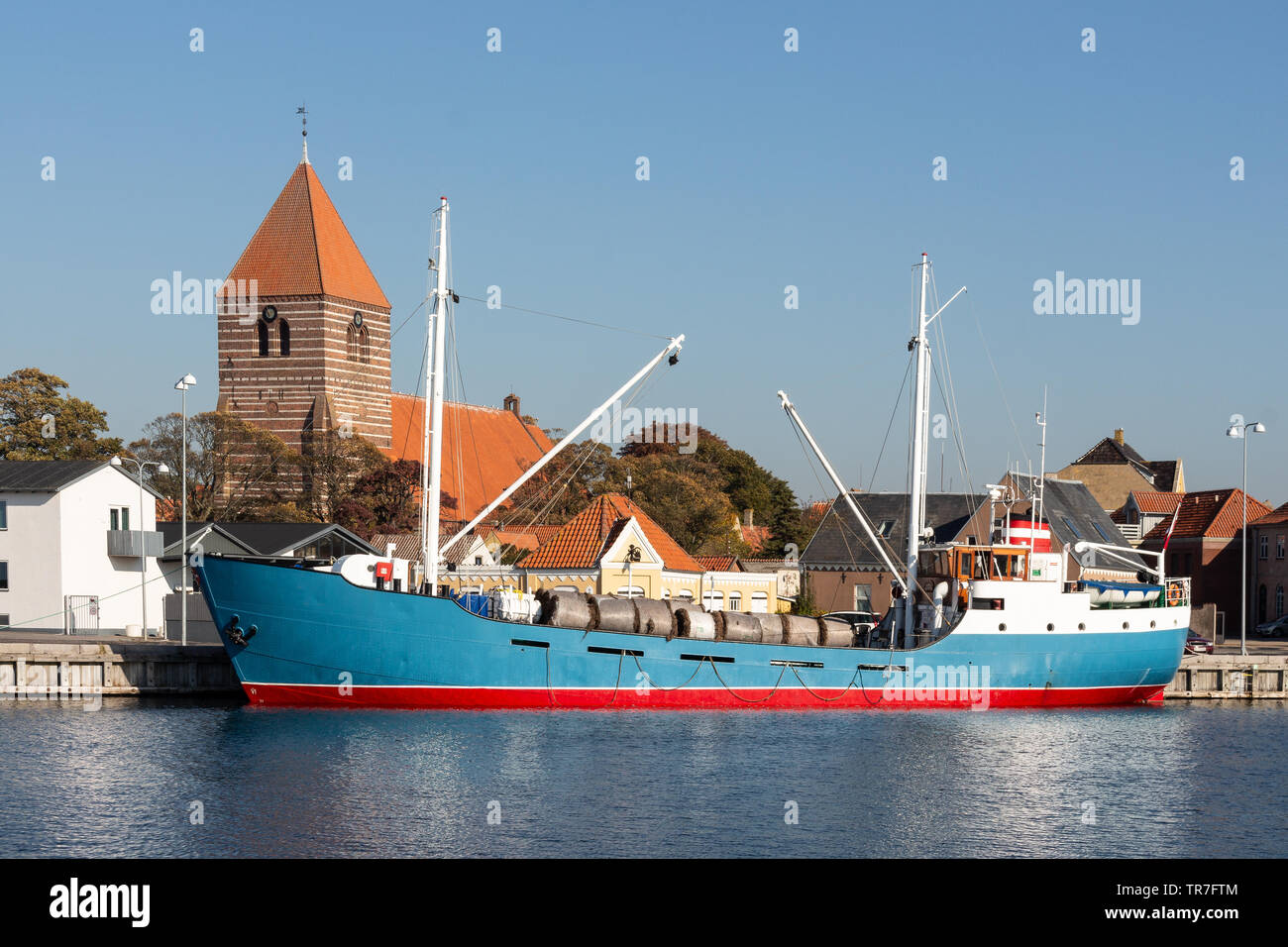 Historische coaster liegend im Hafen von Stege auf der dänischen Insel Moen mit der Kirche des Dorfes im Hintergrund Stockfoto