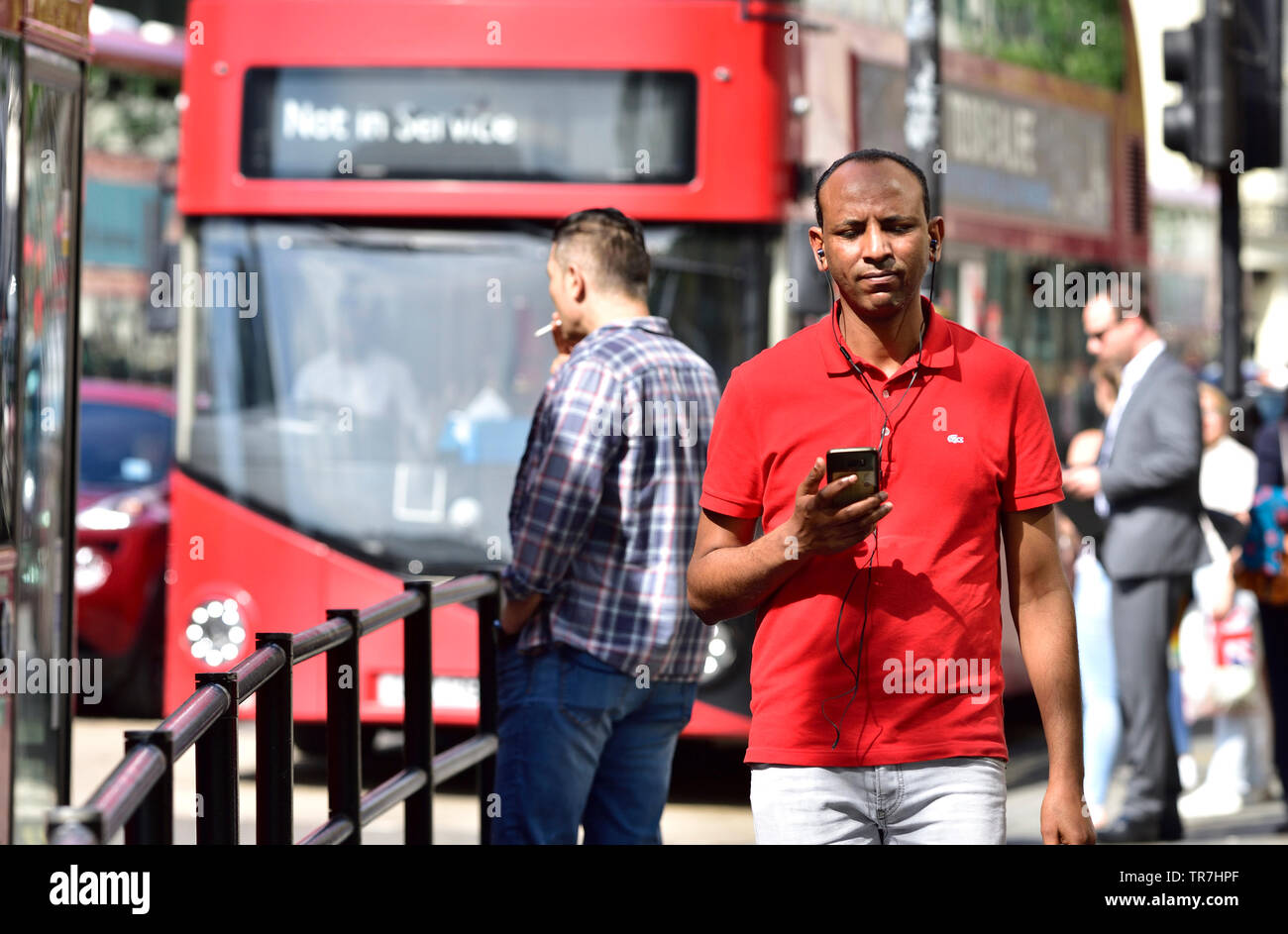 London, England, UK. Mann in einem t-shirt Musik auf sein Handy, Central London Stockfoto