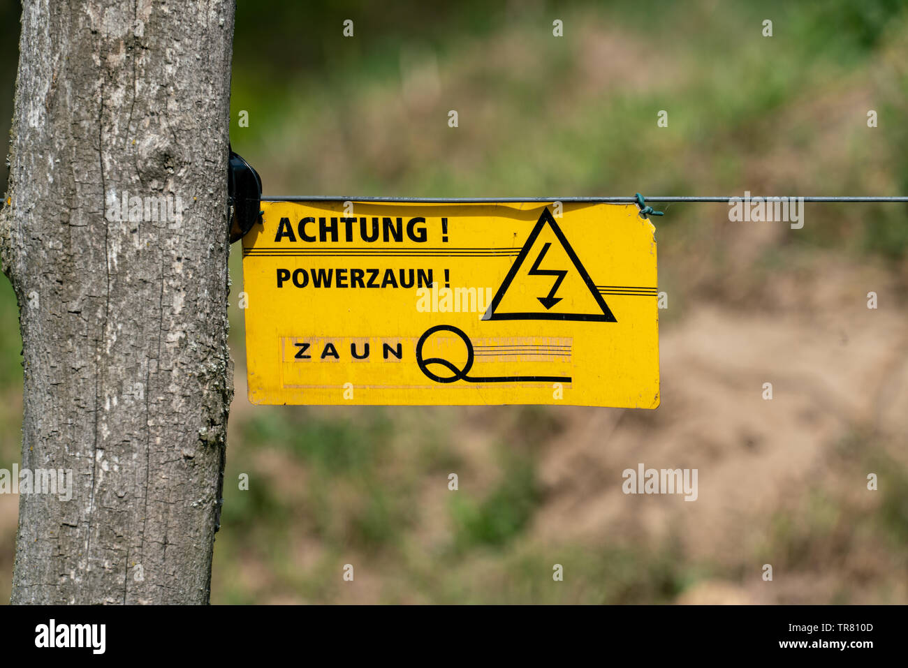 Gelbes Warnschild mit deutschen Wörtern Warnung vor Gefahr und Spannung an einem elektrischen Zaun Stockfoto