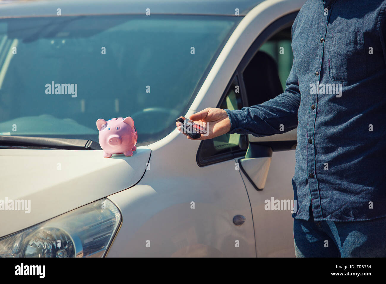Mann draußen mit seinem neuen Auto Schlüssel und Pink piggy Bank Geld auf der Motorhaube. Händler Angebot Credit Finance Services. Auto Leasing, Fahrzeug günstig online Stockfoto