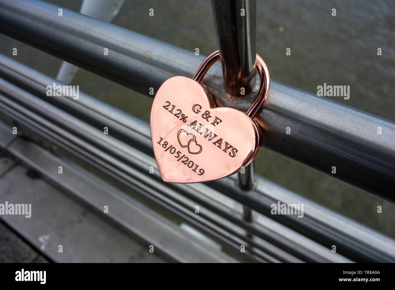Golden personalisiertes Liebesschloss, befestigt an der Hungerford Bridge, London, mit G&F 212% immer 18/05/2019 eingeschrieben auf dem Schloss und zwei Liebesherzen Stockfoto