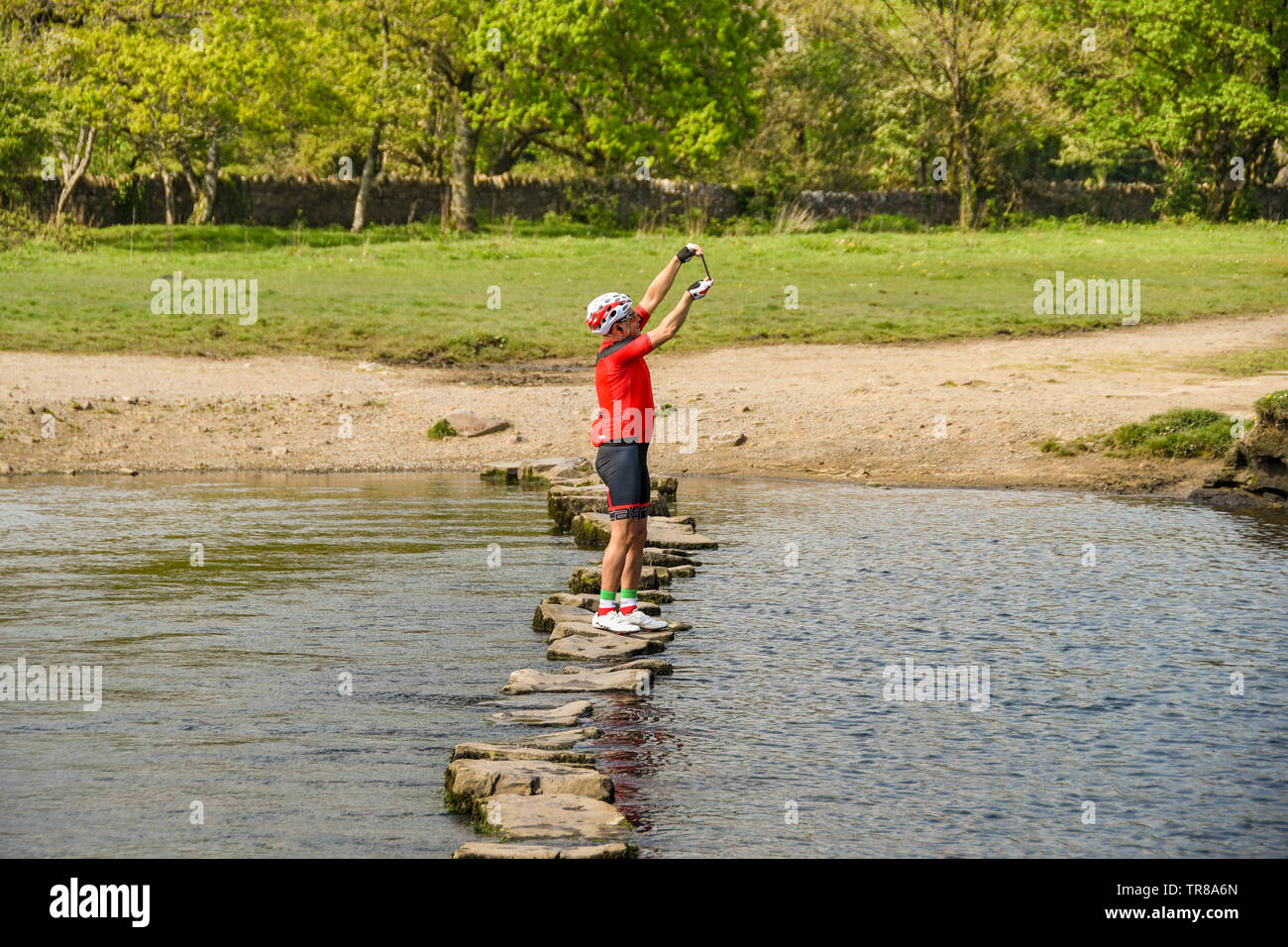 OGMORE VON MEER, WALES - April 2019: Person im cycle Kleidung eine selfie Bild auf einem Mobiltelefon während Balancing auf dem Stepping Stones Stockfoto