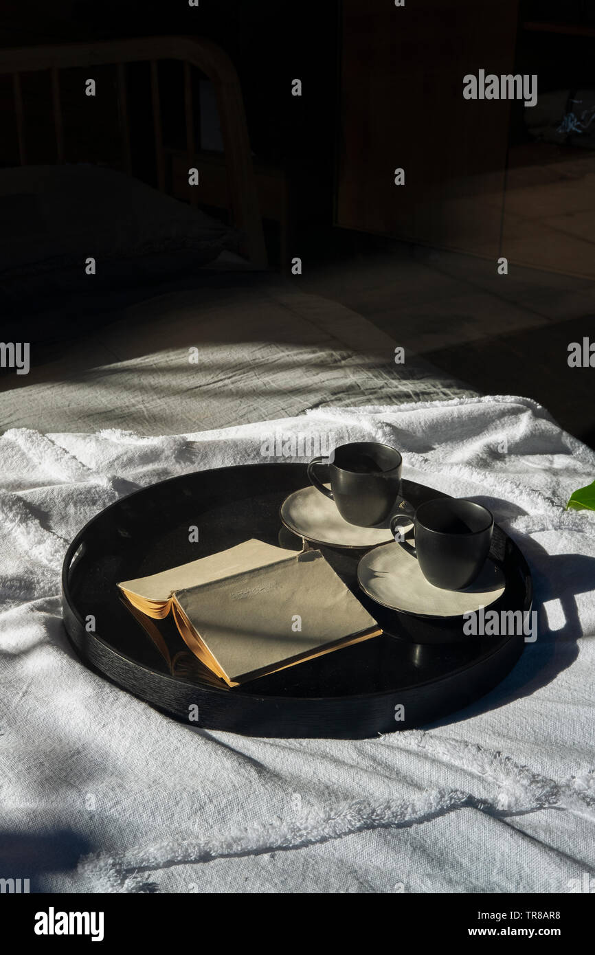 Zwei Tassen und ein Buch auf einem Tablett im Bett - am frühen Morgen Stockfoto