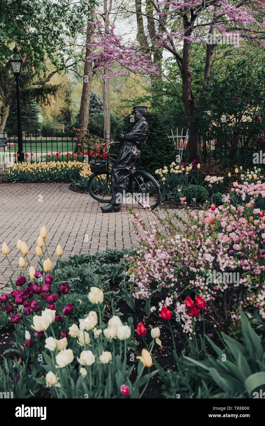 Pella, Iowa, USA - Mai 2, 2019: Skulptur eines niederländischen Mann mit seinem Fahrrad in Scholte Gärten. Vielzahl von Frühlingsblumen und vielfarbigen Tulpen. Stockfoto