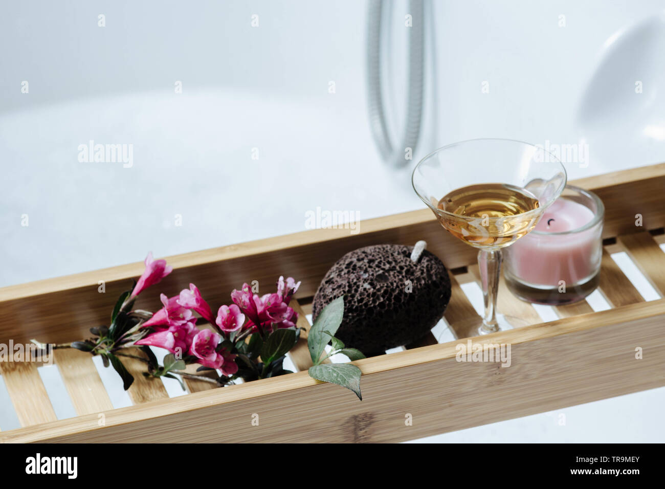 Weiblich - romantisches Bad mit natürlichem Bimsstein, Glas Weißwein, rosa Blumen und Kerzen auf dem Regal für eine Badewanne Stockfoto