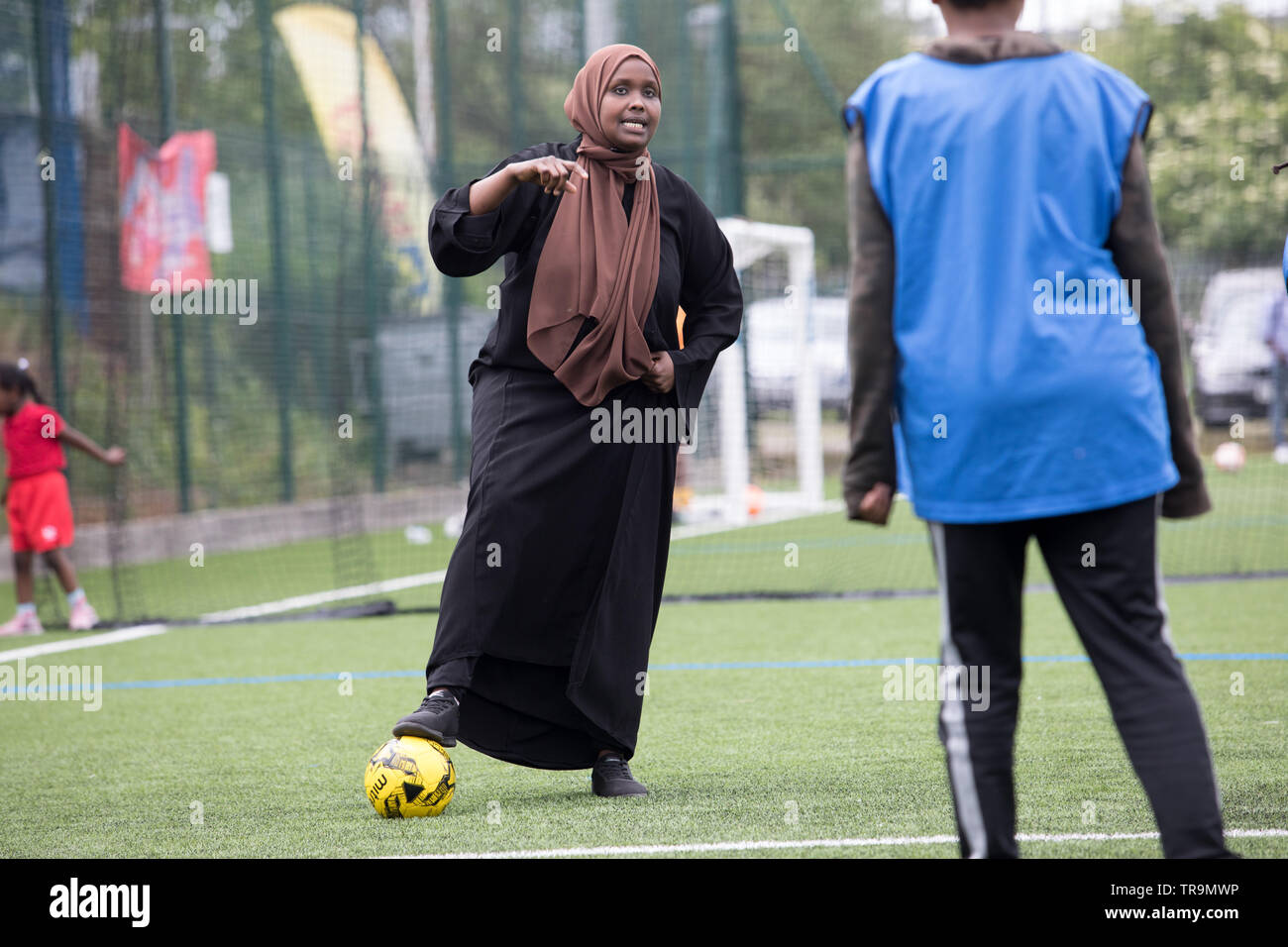 Eine muslimische Frau dribbelt einen Fußball auf Kunstrasen Pitch, bescheiden gekleidet mit einem Kopftuch. Stockfoto