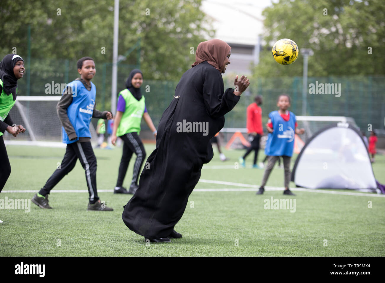 Eine muslimische Mutter Fußball spielen mit Kindern auf einem Kunstrasen Ausbildung Tonhöhe. Stockfoto