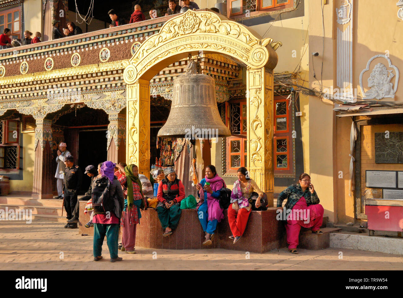 Nepalesische Volk in traditioneller Kleidung sitzen unter großen Glocke vor der tibetisch-buddhistischen Kloster in Boudhanath, Tal von Kathmandu, Nepal Stockfoto