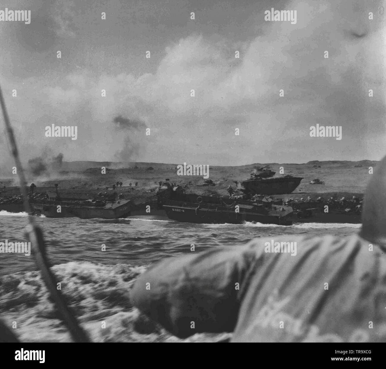 Iwo Battlefield------- vierte Abteilung Marines Überspannungsschutz, vorwärts von dem Strand bei Iwo Jima am D-Day trotz Hagel von Mörtel und Leichte Artillerie, die den hartnäckigen Feind Verteidiger regnen auf den Brückenkopf. Zwei Angriff Wellen sind auf dem Vormarsch, die karge Hang in Richtung der ersten Flugplatz, während eine dritte Angriff Zeile nur den Strand verlassen hat. Andere Wellen warten auf Ihre drehen und noch mehr Truppen in shoreward Landing Craft vorangegangen werden. Stockfoto