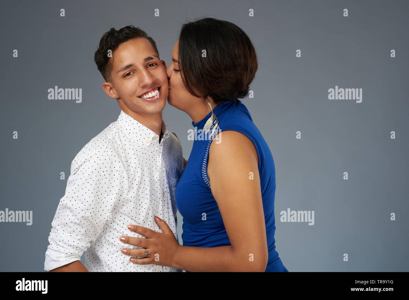Junge Frau küssen Mann auf Grau studio Hintergrund Stockfoto