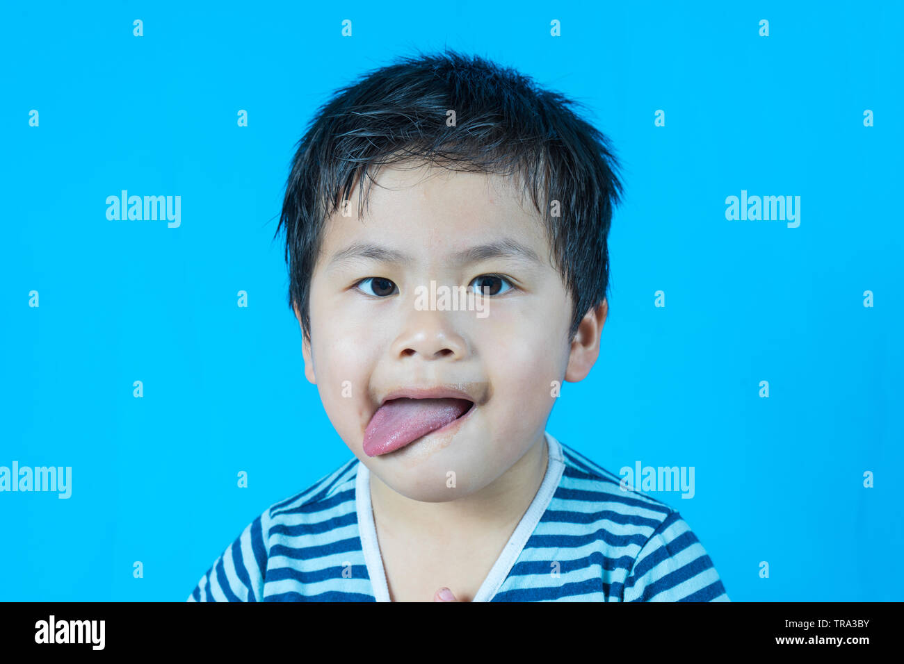 Asiatische cute junge mit Zunge auf blauem Hintergrund, Schokolade schmutzigen Mund, Stockfoto