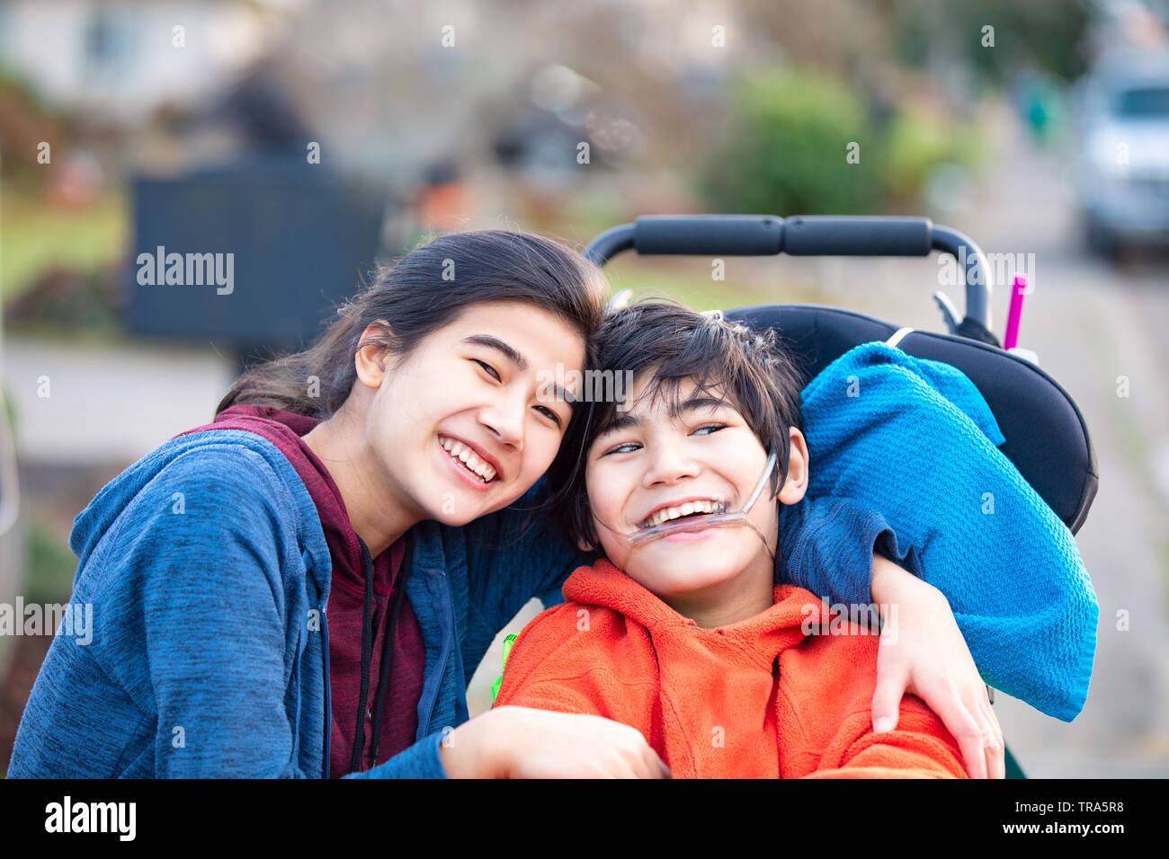 Biracial große Schwester liebevoll umarmen kleine Bruder in wheelchairoutdoors deaktiviert, lächelnd Stockfoto