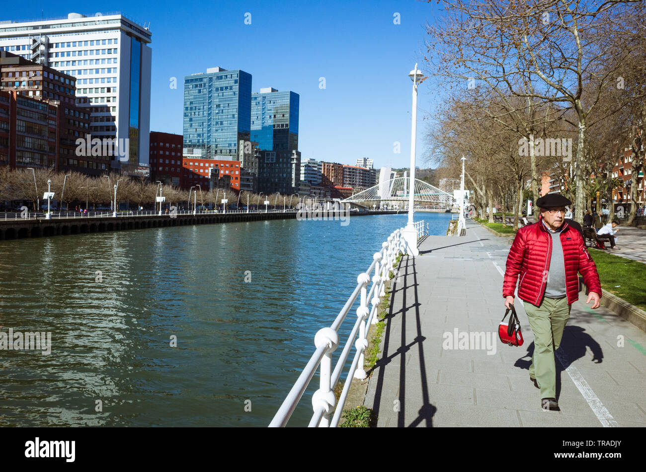 Bilbao, Vizcaya, Baskenland, Spanien: ein Mann mit einem chapela beret Spaziergänge am Fluss Nervion Vergangenheit die moderne Skyline der Stadt. Stockfoto
